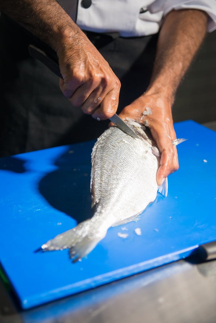 Chef skillfully filleting a fish on a blue cutting board, demonstrating culinary expertise.